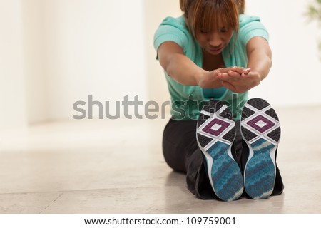 Cute Filipino woman exercising in a living room wearing a green shirt, black pants and tennis shoes.