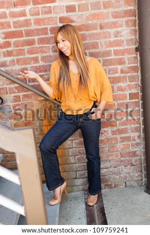 Beautiful Filipino woman outdoors wearing a gold shirt, blue jeans and beige high heels.
