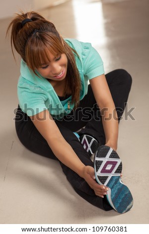 Cute Filipino woman exercising in a living room wearing a green shirt, black pants and tennis shoes.