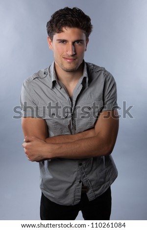 Handsome young white man in studio wearing grey shirt on grey background with dark brown hair.