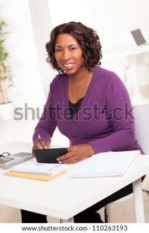 Beautiful African American female executive with dark brown hair at work in an office setting wearing a purple sweater.