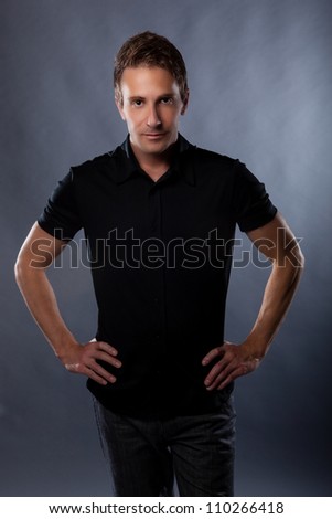 Good looking Caucasian guy in studio on gray background wearing modern black shirt.