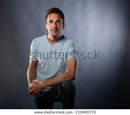 Handsome white man photographed in studio on a gray background wearing a modern blue t shirt and jeans.