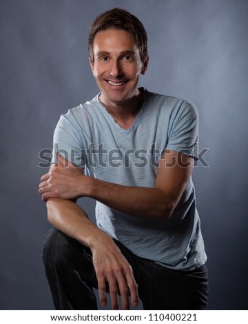 Handsome white man photographed in studio on a gray background wearing a modern blue t shirt and jeans.