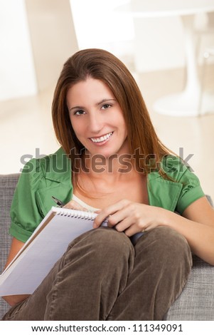 Beautiful young female sitting on gray chair writing on pad of paper.