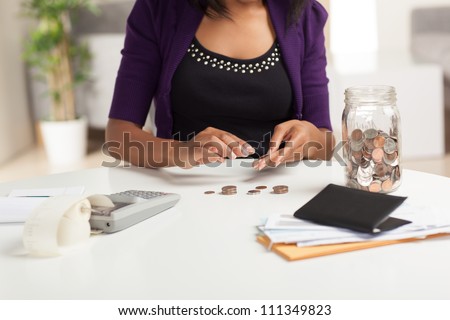 Attractive young African American woman working on finances at home wearing purple jacket sitting at dining table.