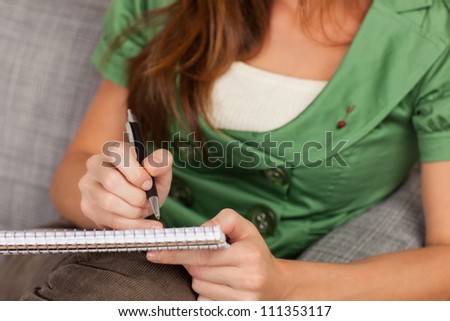 Beautiful young female sitting on gray chair writing on pad of paper.