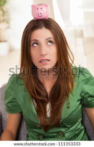 Attractive young female sitting on chair at home with cute pink piggy bank.