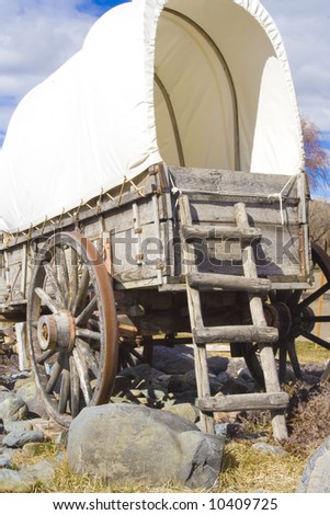 A rear view of a covered wagon used on the Old Oregon Trail. It has  a weathered wooden ladder leaning on it.