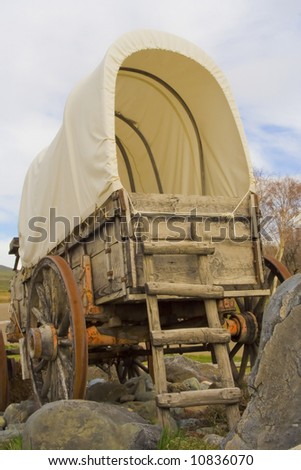 An old covered wagon sits on a rocky patch of ground.