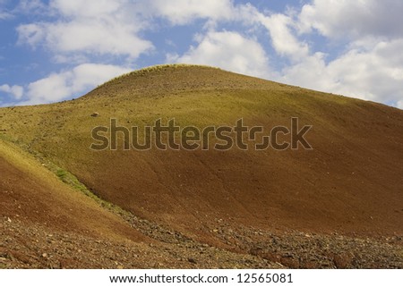 A towering hill from the Oregon Painted hills shows two ancient climate changes as evidenced by the two colors in the stone and reaches toward a beautiful blue sky.