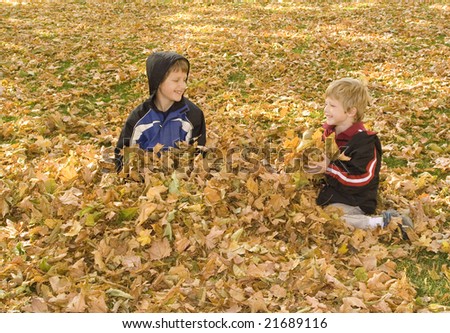 Two boys playing in a leaf pile and smiling.
