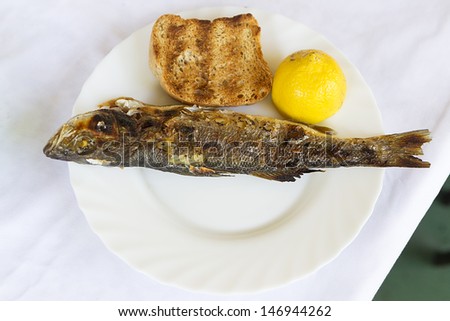 Grilled seabass fish served in a dish with a slice of bread and a lemon