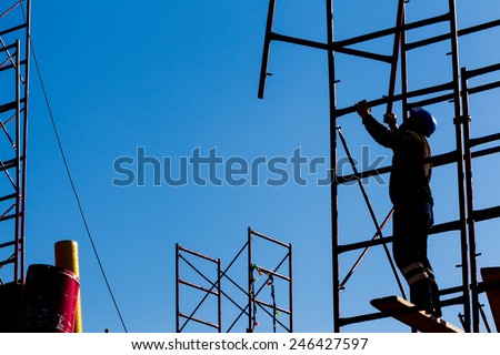 silhouette of construction worker against sky on scaffolding with ladder on building site
