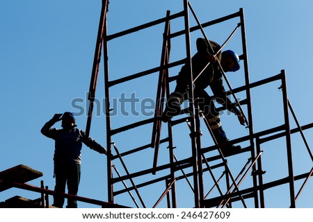 silhouette of construction workers against sky on scaffolding with ladder on building site