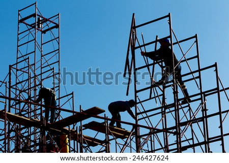 silhouette of construction workers against sky on scaffolding with ladder on building site