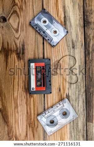 Vintage audio cassette with loose tape shaping one heart on a wooden background.