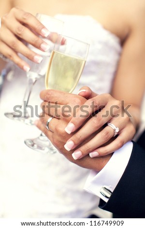 Wedding couple holding hands with champagne glasses showing off the new rings