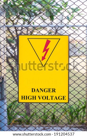 warning sign posted on the fence surrounding large electrical transformers.