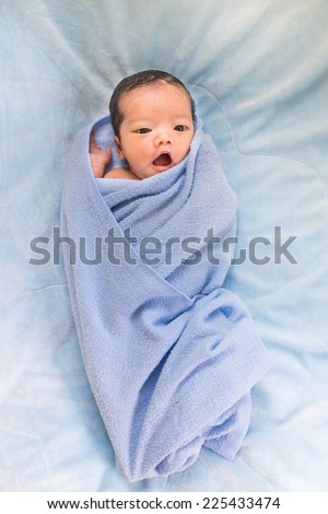 Newborn baby girl lying on his back relaxing under a blue wrap cloth