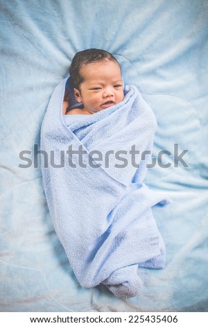 Newborn baby girl lying on his back relaxing under a blue wrap cloth