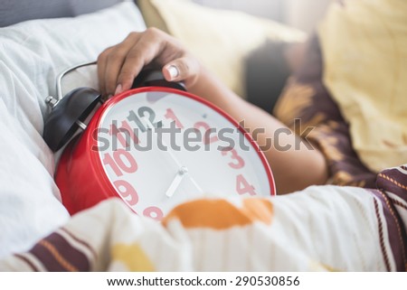 Hand under blanket reaching out for alarm clock in bedroom with men sleeping