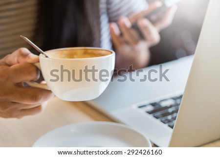 Close up of coffee cup ,background of woman using her cell phone in coffee shop,cafe