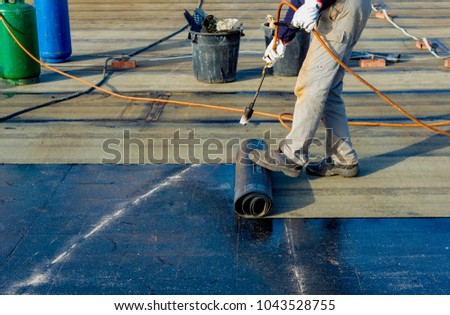Worker preparing part of bitumen roofing felt roll for melting by gas heater torch flame. On the back of the sheath there is the stamp  \