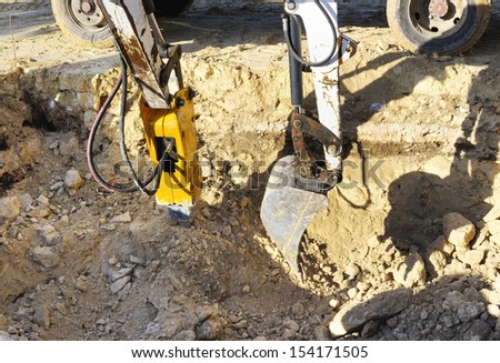 Two excavators in action to perform an excavation in rock. One with hydraulic hammer destroys the rock and the other with the machine loads a truck