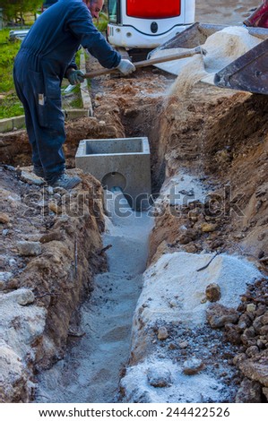 Excavator electrical conduits covered with sand with the assistance of a worker. Motion blur