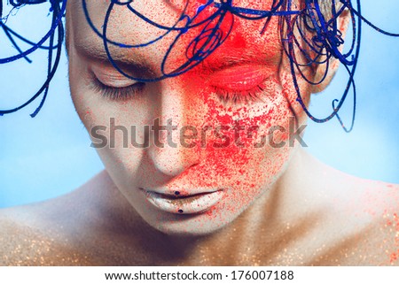 horizontal portrait of sexy woman with neon powder on face in studio on blue background