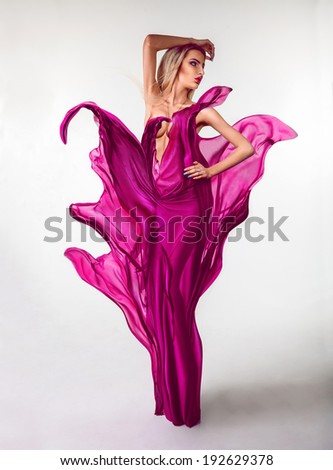 Voluptuous young woman with creative pink dress in studio on grey background