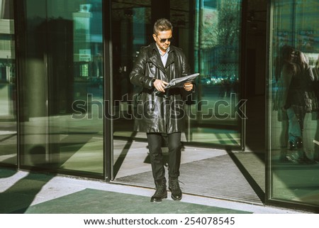 adult glamour man walks out of doors with newspaper in hands outdoors