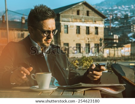 Horizontal portrait of working business man with mobile phone and cup of coffee on table outdoors