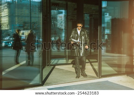 Man with newspaper in hand walks out of doors outdoors