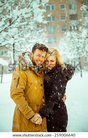Vertical photo of betrothed couple in love looking at camera and smiling in the snow. Color and high contras image