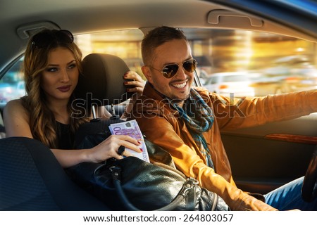 smiling fashionable man is driving at full speed with a stunning girl in the back seat and a bag full of money in the middle. Inside photo