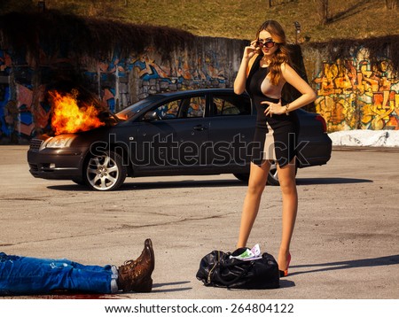 Gorgeous young adult female stand near bag full of money behind burning car outdoors