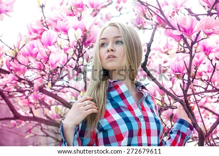 dreamy blonde girl looking to the side near the spring blooming trees outdoor at park