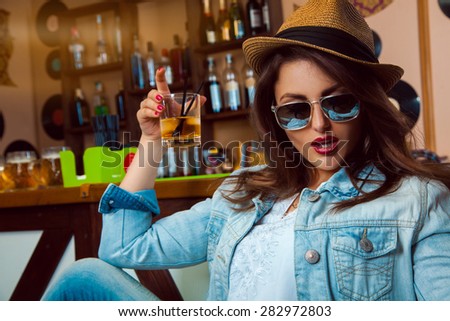 Lovely adult female in sunglasses with make up and healthy skin drink cocktail in bar. horizontal photo
