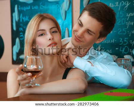 pretty girl with glass of wine and hugs her boyfriend from behind at bar. horizontal photo