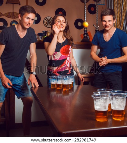Beautiful brunette girl having fun with twins playing beer pong. Square photo