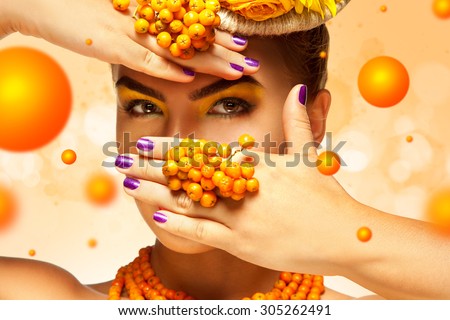 Beautiful shy fashion girl hide face beahind hand with rowan accessories on orange background