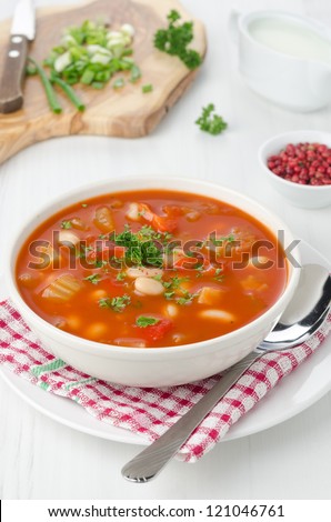 bowl of roasted tomato soup with beans, celery and sweet pepper garnished with fresh parsley, pink pepper and sour cream in the background