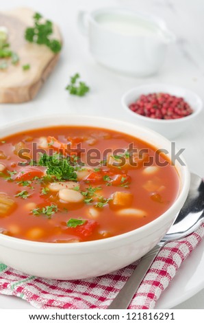 bowl of roasted tomato soup with beans, celery and bell pepper, pink pepper and sour cream in the background