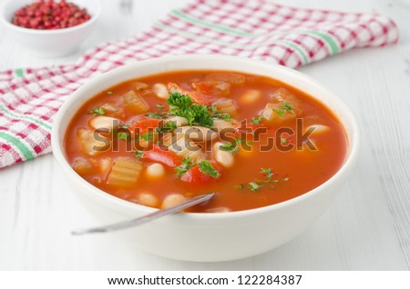 bowl of roasted tomato soup with beans, celery and bell pepper, closeup horizontal, pink pepper in the background