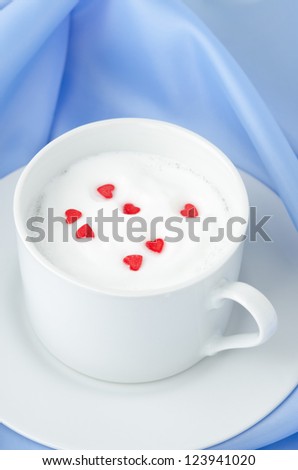 cup of hot milk foam and sugar hearts on a blue background