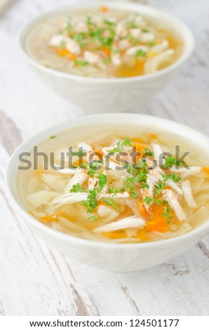 two bowls of vegetable soup with chicken and parsley closeup