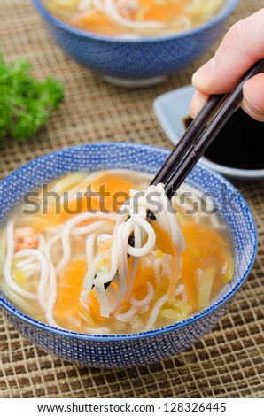 Chinese soup with noodles and vegetables and hand with chopsticks