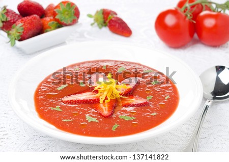 tomato and strawberry gazpacho in a plate, fresh berries and tomatoes in the background